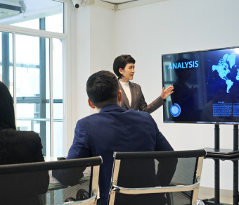 Woman presenting analysis on screen to people sitting at conference table