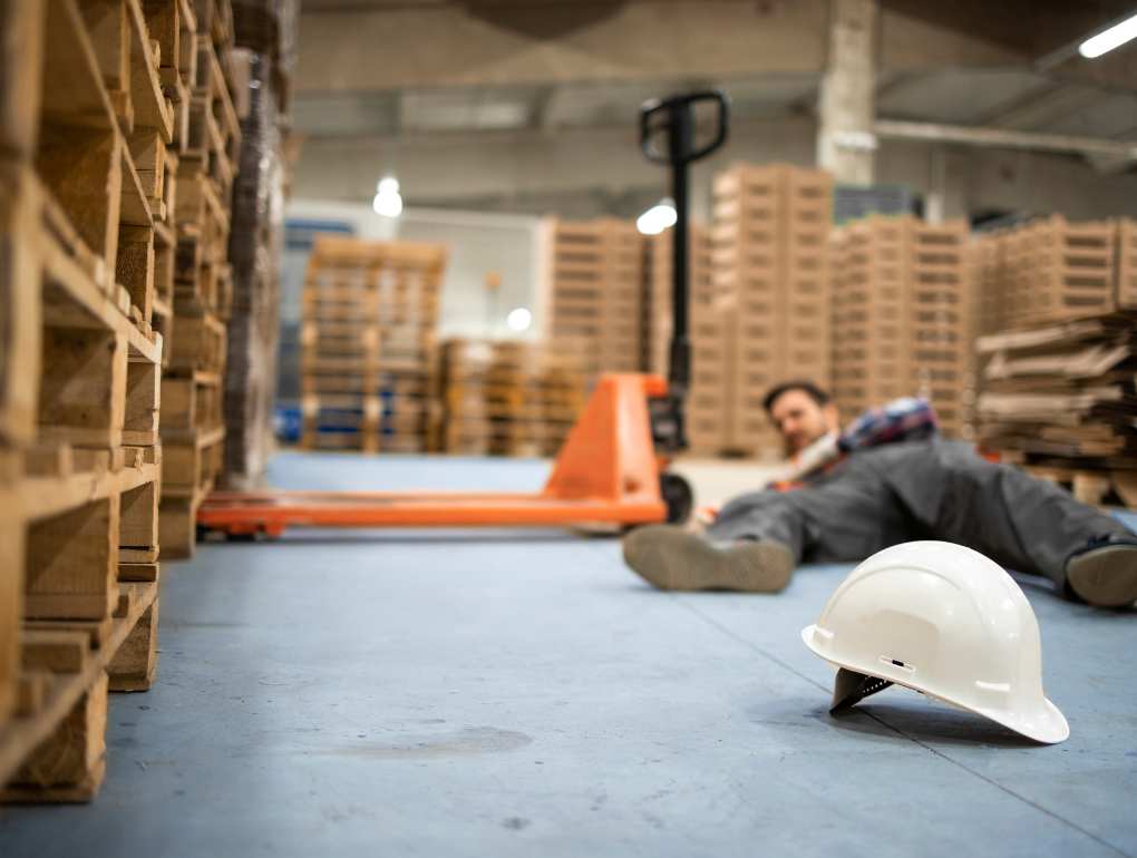 Man on ground next to pallet jack with white helmet on the ground next to him